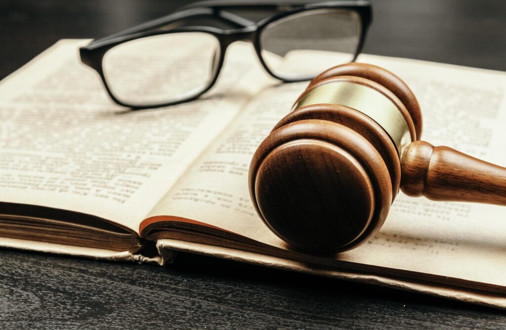 Sanz Bremond Abogados, asesoría legal integral en derecho penal y administrativo en Burriana. Un mallete y unas gafas sobre el mismo libro.